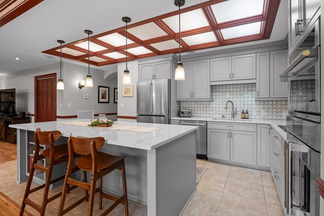kitchen with decorative backsplash, a center island, a sink, gray cabinetry, and stainless steel appliances