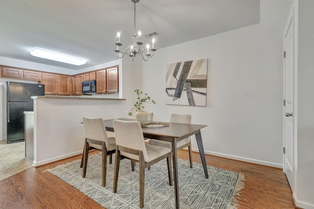 dining area with baseboards, a notable chandelier, light wood finished floors, and visible vents