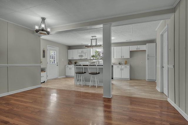 kitchen featuring white microwave, light wood-style flooring, white cabinetry, and a notable chandelier