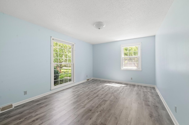 empty room with baseboards, a textured ceiling, visible vents, and wood finished floors