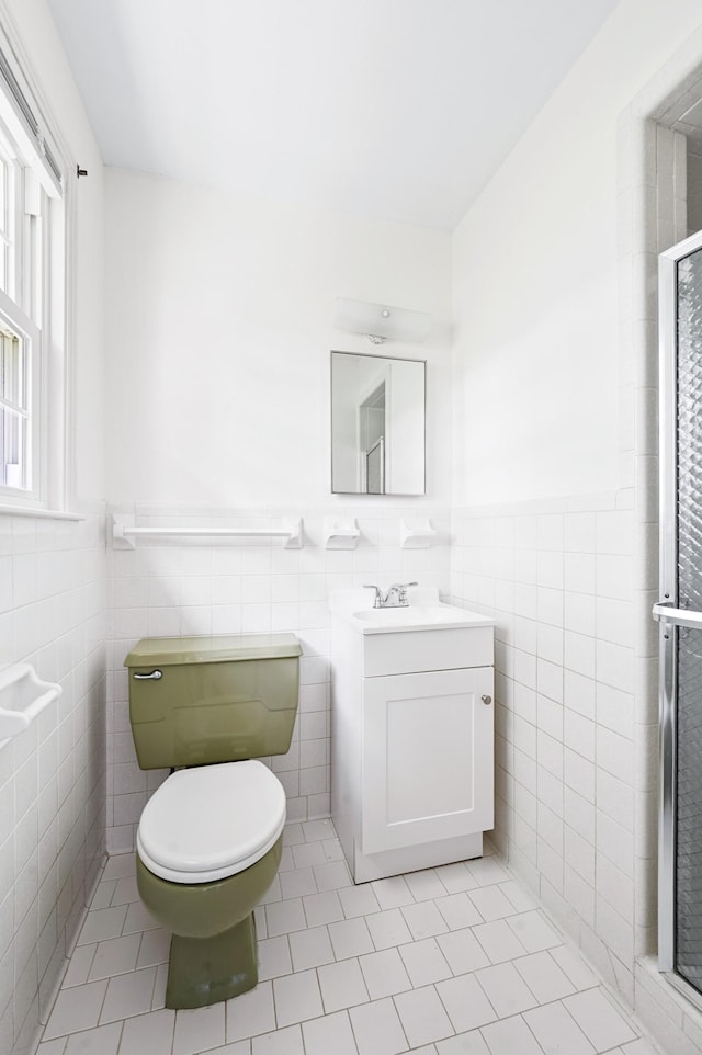 full bath with vanity, toilet, tile patterned floors, a wainscoted wall, and tile walls