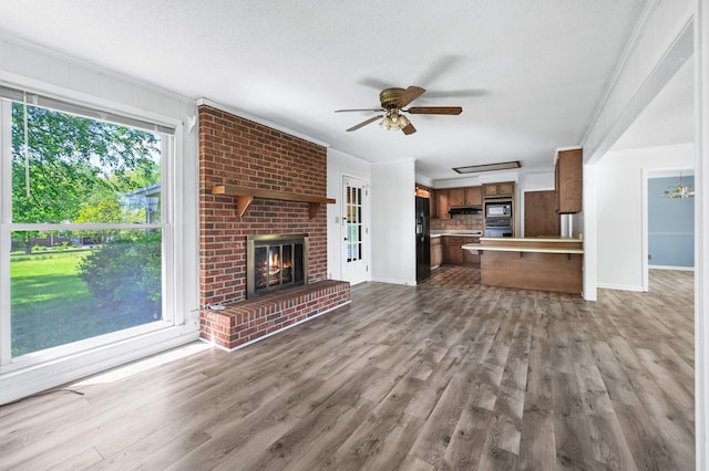 unfurnished living room with ceiling fan, a brick fireplace, baseboards, wood finished floors, and ornamental molding