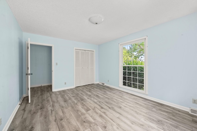 unfurnished bedroom with baseboards, visible vents, wood finished floors, and a closet