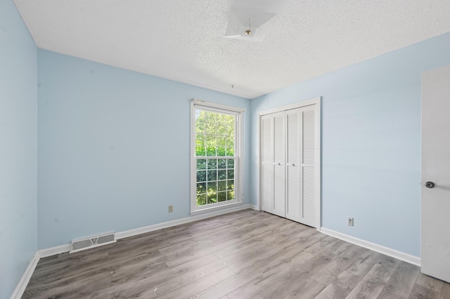 unfurnished bedroom featuring visible vents, a closet, wood finished floors, baseboards, and a textured ceiling
