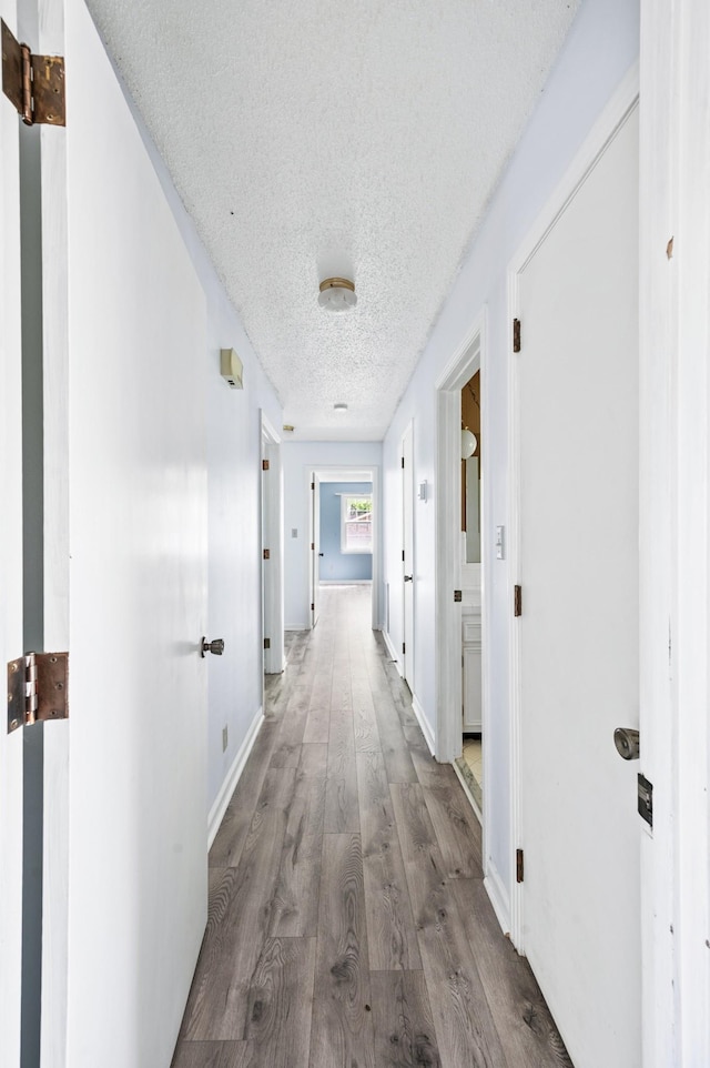 hallway featuring baseboards, a textured ceiling, and wood finished floors