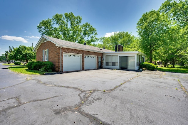 view of side of home featuring an attached garage, a chimney, driveway, and brick siding