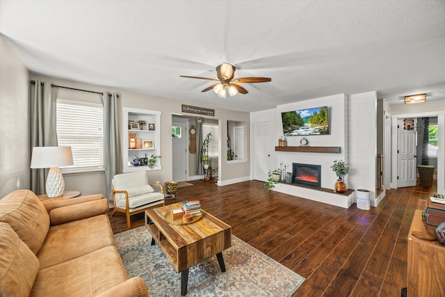 living area with baseboards, a ceiling fan, a glass covered fireplace, and wood finished floors