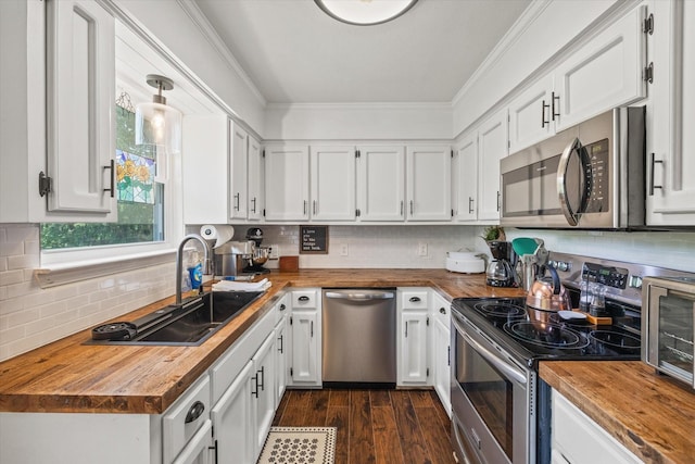 kitchen with crown molding, appliances with stainless steel finishes, a sink, butcher block counters, and white cabinetry