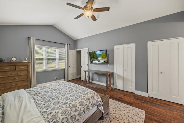 bedroom featuring a ceiling fan, baseboards, two closets, lofted ceiling, and dark wood-type flooring