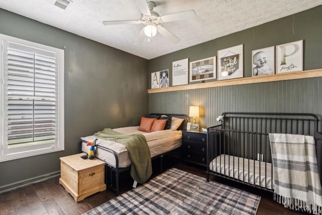 bedroom with baseboards, a textured ceiling, visible vents, and wood finished floors