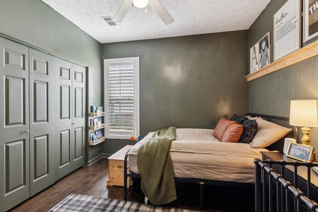 bedroom with a ceiling fan, a textured ceiling, visible vents, dark wood finished floors, and a closet
