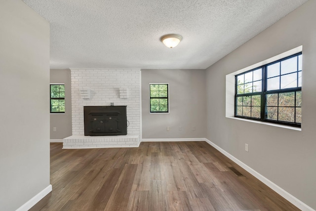 unfurnished living room featuring a brick fireplace, a textured ceiling, baseboards, wood finished floors, and visible vents