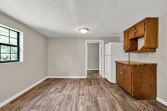 kitchen featuring brown cabinets, a textured ceiling, dark wood finished floors, freestanding refrigerator, and baseboards