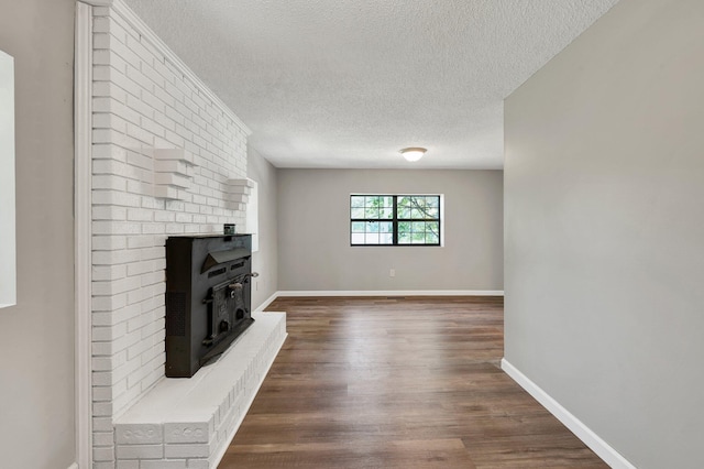 unfurnished living room featuring baseboards, a wood stove, dark wood-style floors, and a textured ceiling