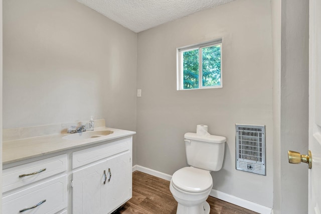 half bath featuring vanity, heating unit, wood finished floors, toilet, and a textured ceiling