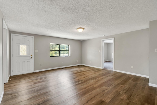 unfurnished living room featuring dark wood-type flooring, a textured ceiling, and baseboards