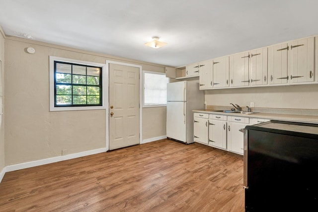 kitchen featuring freestanding refrigerator, baseboards, light countertops, a sink, and light wood-style flooring