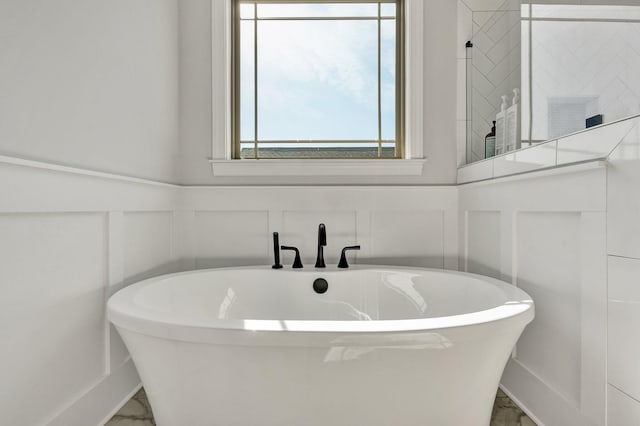 full bath with a soaking tub, marble finish floor, and a decorative wall