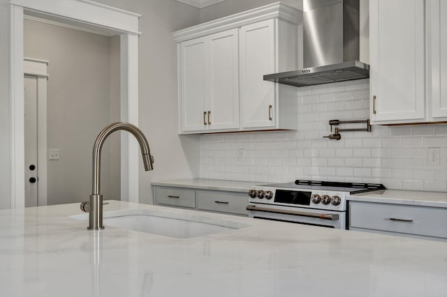 kitchen with a sink, light stone countertops, range with electric cooktop, and wall chimney exhaust hood