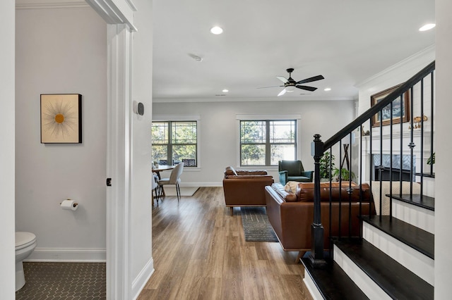 living room featuring ceiling fan, baseboards, wood finished floors, ornamental molding, and stairway