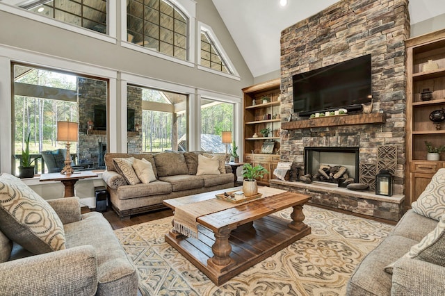 living area with high vaulted ceiling, a stone fireplace, and wood finished floors