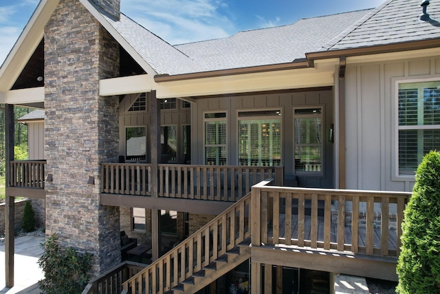 property entrance with board and batten siding, a wooden deck, a shingled roof, and a chimney