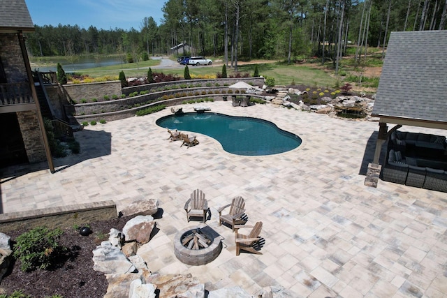 view of pool featuring an outdoor fire pit, a fenced in pool, a water view, a patio area, and a wooded view