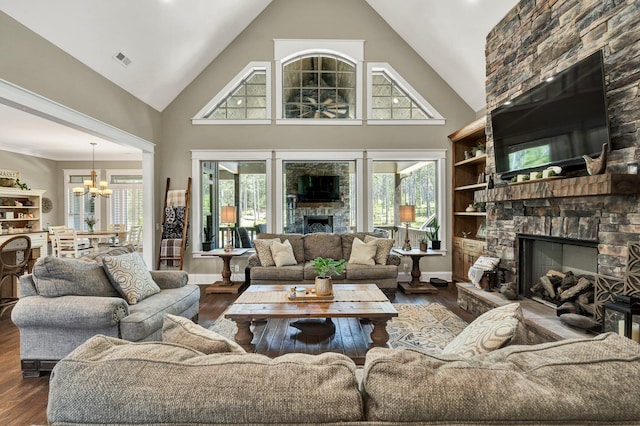 living area featuring visible vents, wood finished floors, a stone fireplace, high vaulted ceiling, and a notable chandelier