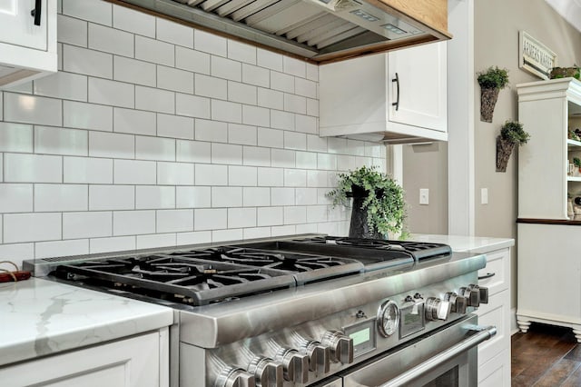 kitchen with high end range, white cabinets, custom range hood, and tasteful backsplash