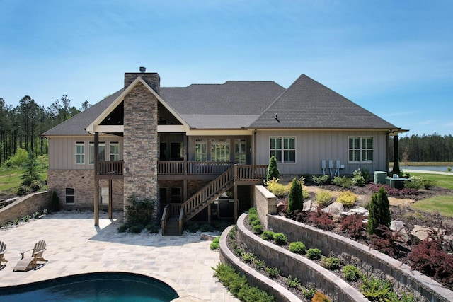 rear view of house featuring board and batten siding, roof with shingles, a chimney, and a patio area