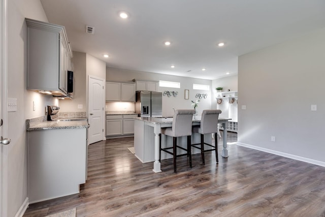 kitchen featuring a kitchen island, dark wood-style flooring, stove, stainless steel fridge, and a breakfast bar