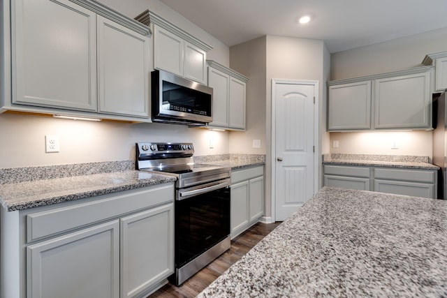 kitchen with dark wood-style flooring, appliances with stainless steel finishes, gray cabinets, and light stone counters