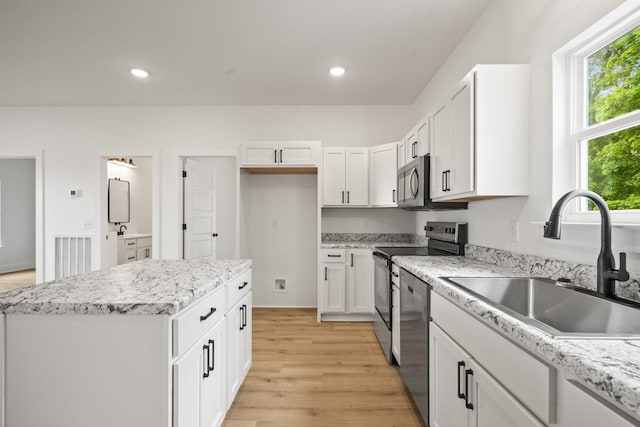 kitchen with appliances with stainless steel finishes, a sink, light wood-style floors, white cabinetry, and a kitchen island