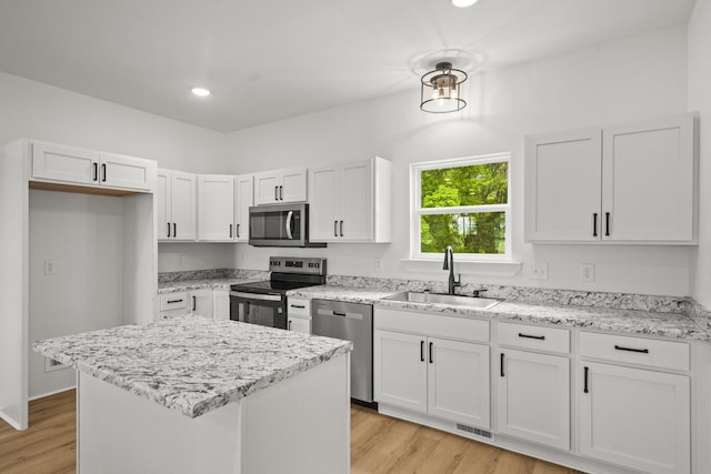 kitchen with appliances with stainless steel finishes, a sink, light wood finished floors, white cabinetry, and visible vents