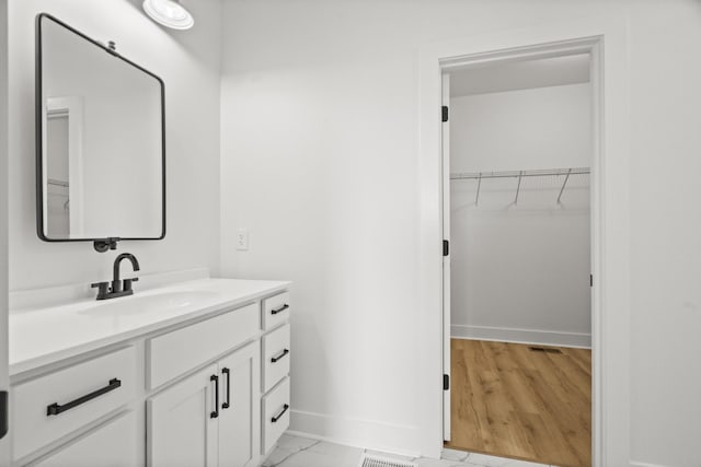 bathroom with baseboards, visible vents, a spacious closet, and vanity