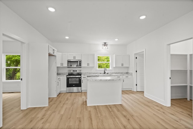 kitchen with a sink, white cabinets, light wood-style floors, and stainless steel appliances
