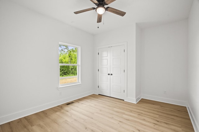 unfurnished bedroom featuring a ceiling fan, visible vents, light wood-type flooring, baseboards, and a closet