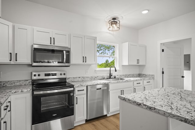 kitchen with white cabinets, light stone counters, a sink, stainless steel appliances, and electric panel