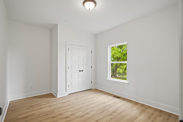 unfurnished bedroom featuring baseboards, a closet, light wood finished floors, and visible vents