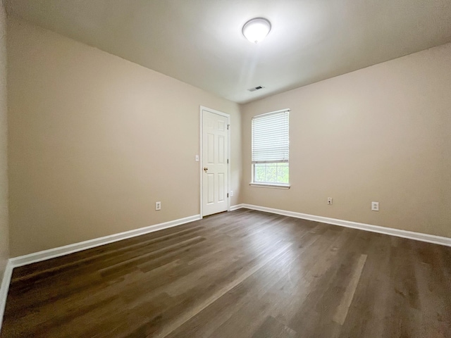 unfurnished room featuring baseboards, dark wood finished floors, and visible vents