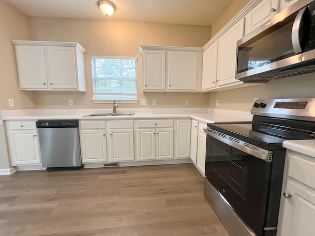 kitchen with light wood-style floors, a sink, white cabinetry, and appliances with stainless steel finishes