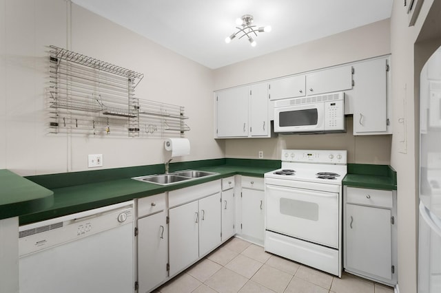 kitchen featuring dark countertops, a sink, light tile patterned floors, white cabinets, and white appliances