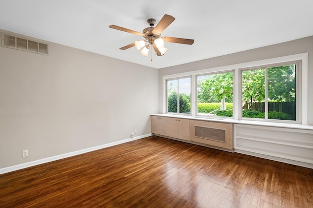 empty room with a ceiling fan, baseboards, visible vents, and dark wood finished floors