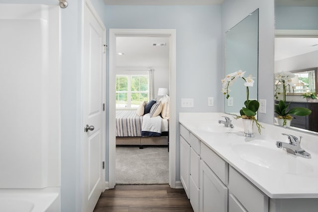 bathroom featuring double vanity, ensuite bath, a sink, and wood finished floors