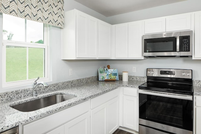 kitchen with stainless steel appliances, light stone counters, white cabinetry, and a sink