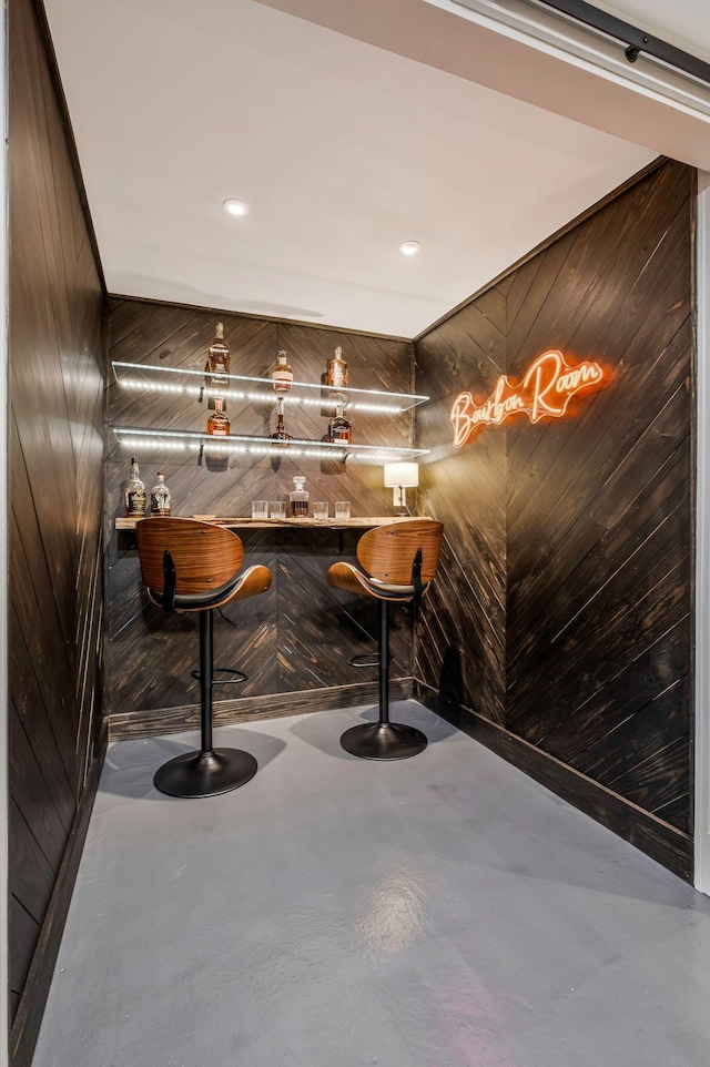bar featuring finished concrete flooring, a community bar, and wood walls