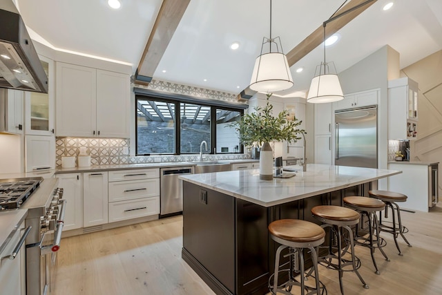 kitchen featuring light stone counters, a center island, white cabinetry, high end appliances, and range hood