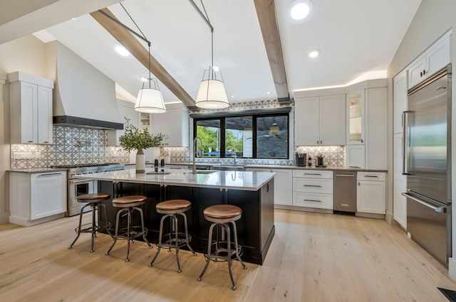 kitchen featuring high quality appliances, lofted ceiling with beams, light wood-style flooring, custom range hood, and tasteful backsplash