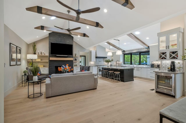 living area with wine cooler, a fireplace, a ceiling fan, and light wood finished floors