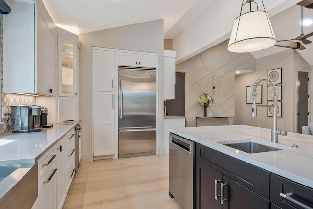 kitchen featuring decorative backsplash, a sink, light wood finished floors, stainless steel appliances, and white cabinetry